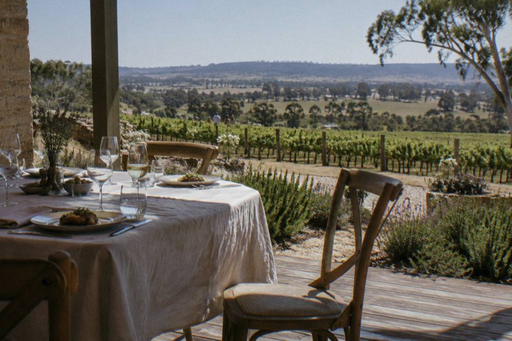 A set table with wine glasses and plated food overlooking Barossa vineyards